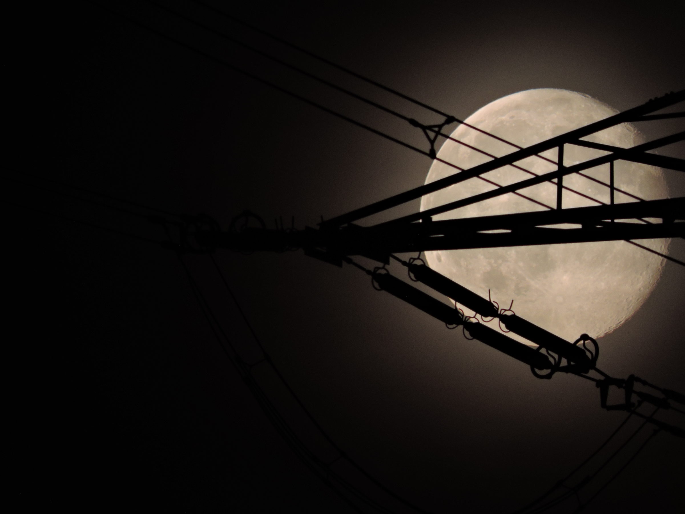 Hochspannungsmast bei Nacht mit Vollmond im Hintergrund